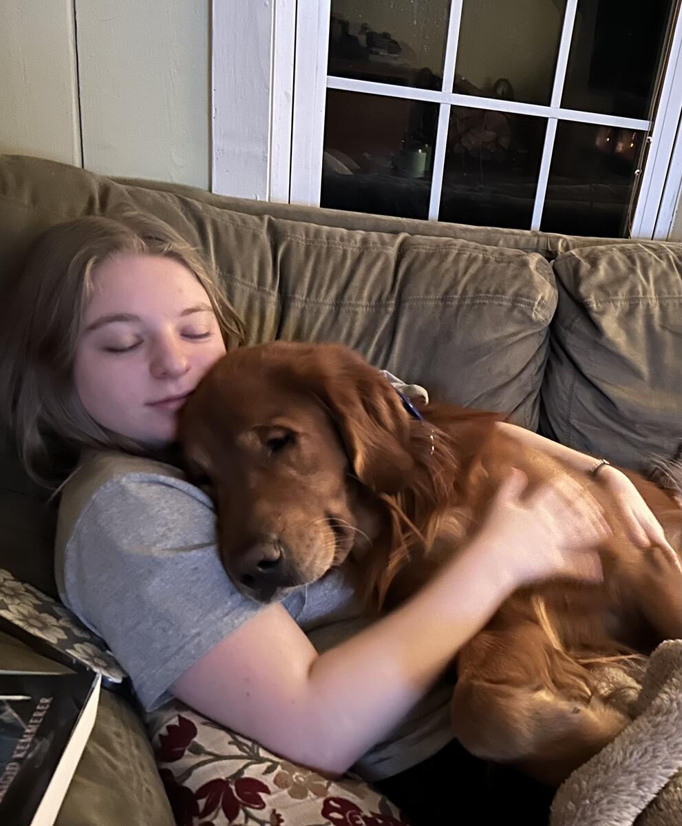 White woman with blonde hair sleeping on a couch with an adorable golden retriever