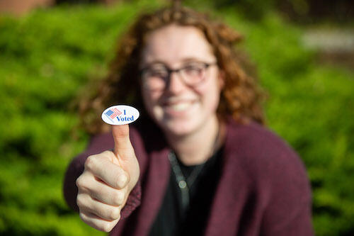 A student shows an "I voted" sticker from a previous year.