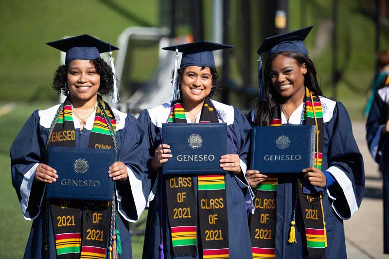 Three women graduates hold their SUNY Geneseo degrees at Commencement 2021
