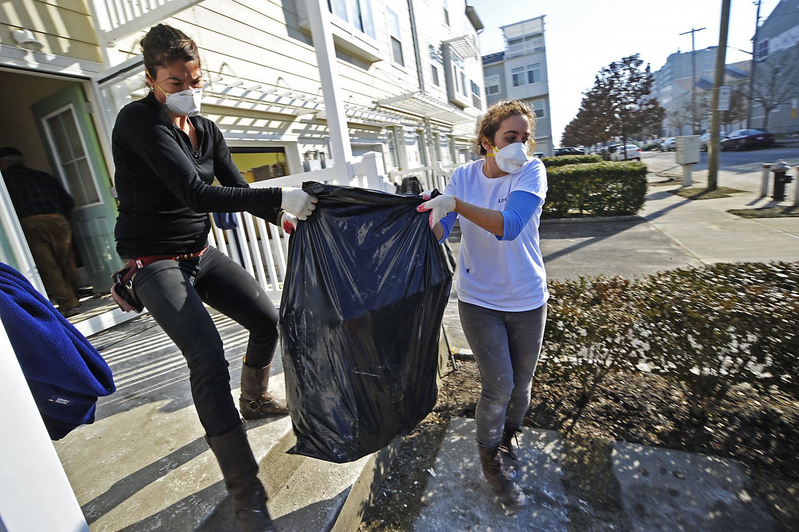 two women carrying a full garbage bag