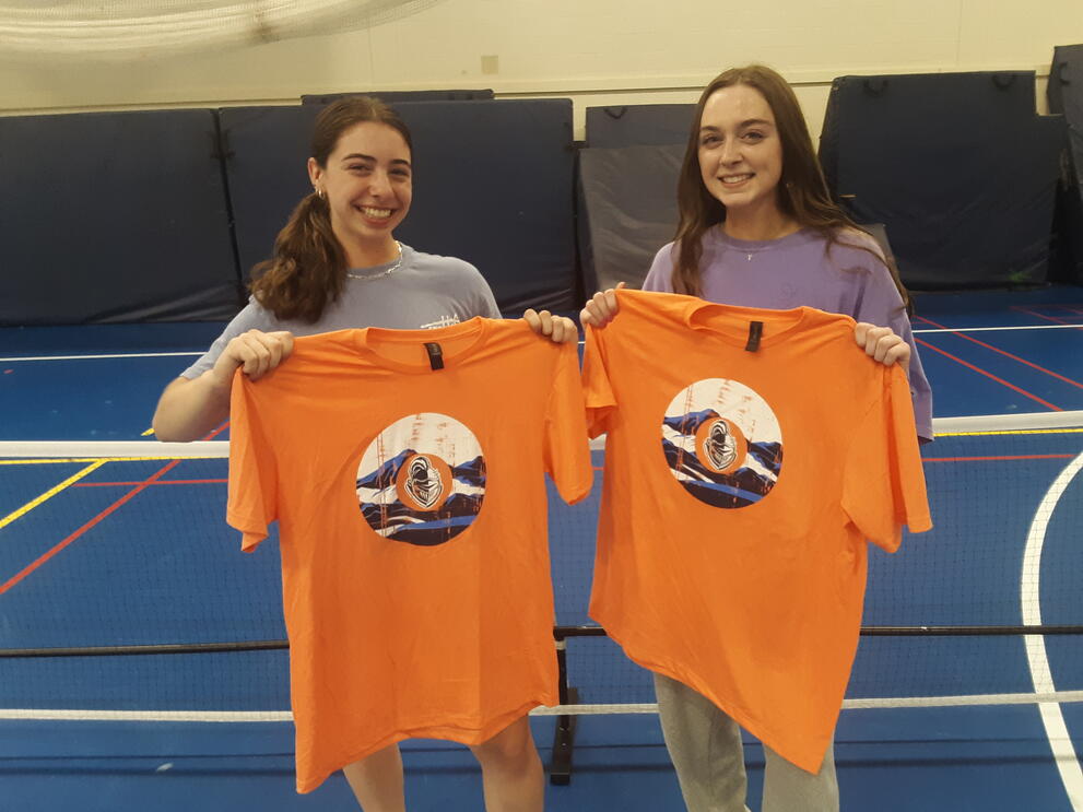 Two pickleball champions holding orange uniforms