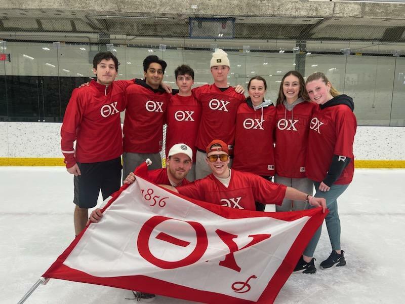 Nine broomball champions wearing red uniforms and holding the team flag