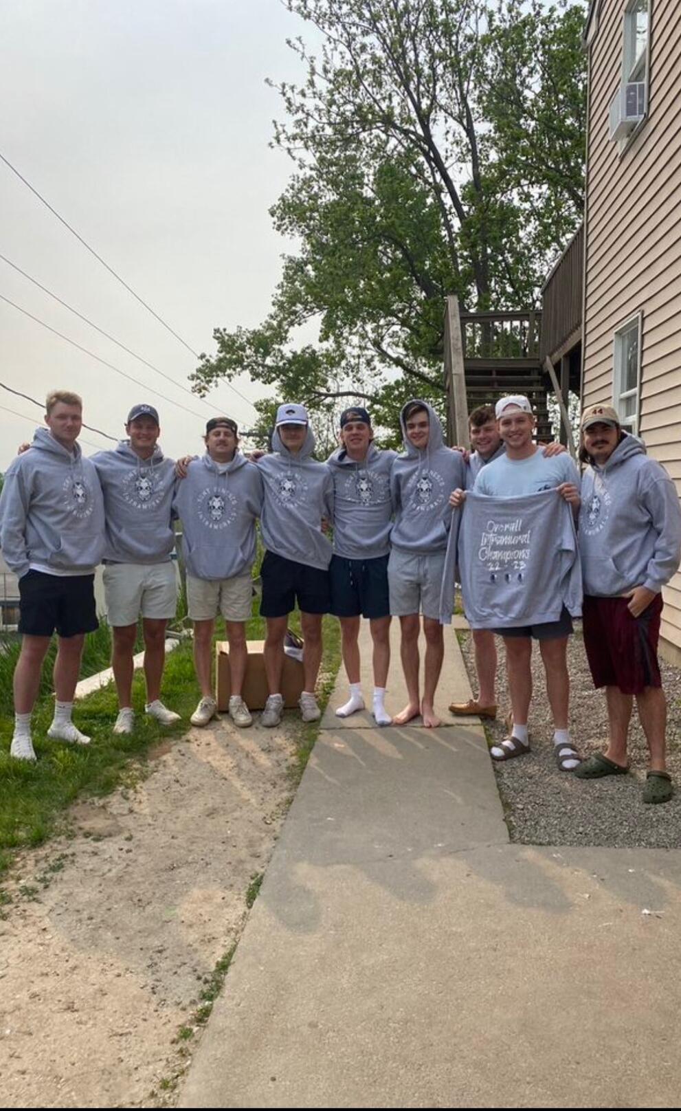 Eight athletes wearing gray uniforms and standing together outside