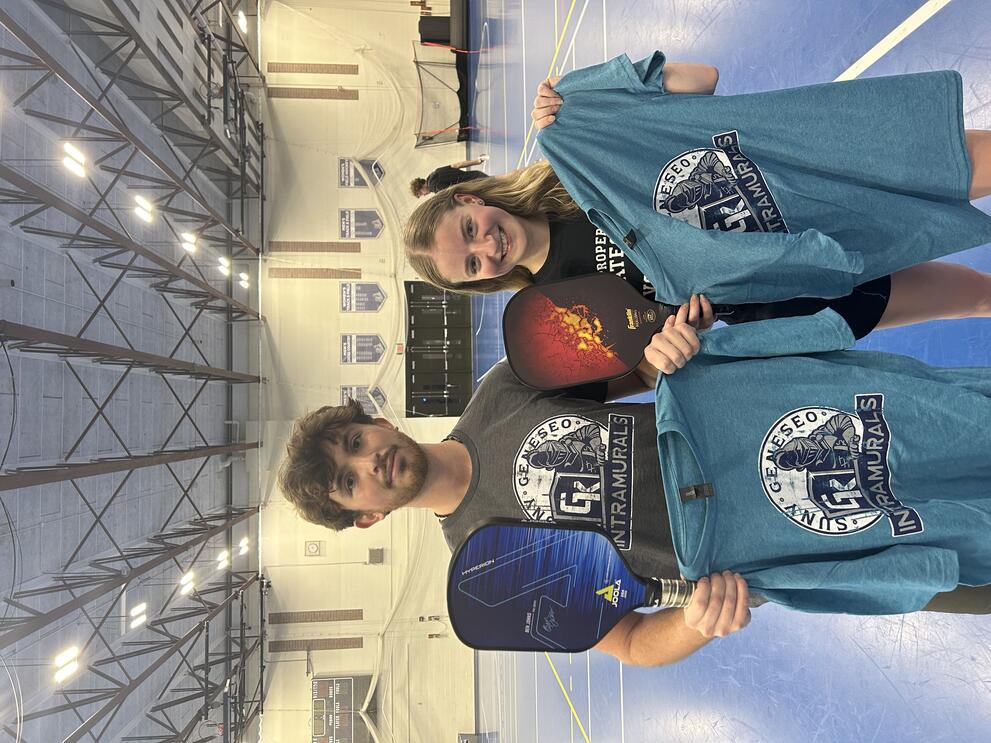 2 pickleball champions holding blue intramural t-shirts.