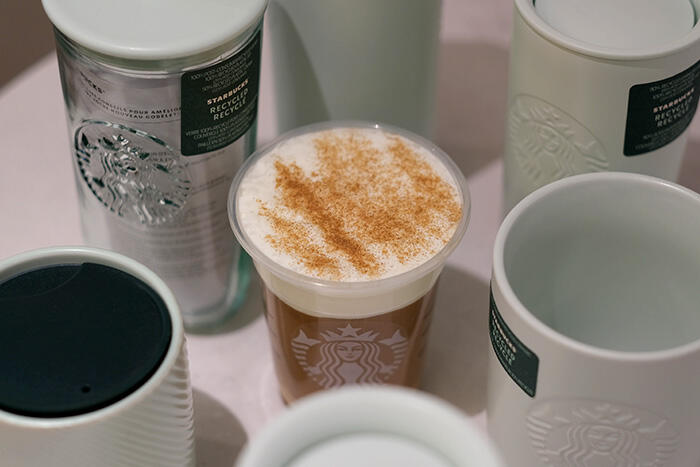 A signature drink with cinnamon cold foam surrounded by reusable Starbucks drinkware.