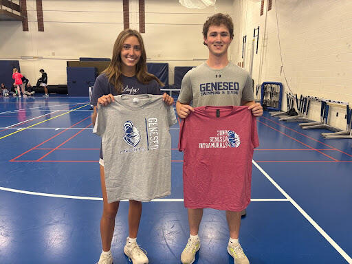 Two students standing on an indoor gym court holding T-shirts, one gray and one red, both printed with “SUNY Geneseo Intramurals” and a volleyball graphic.