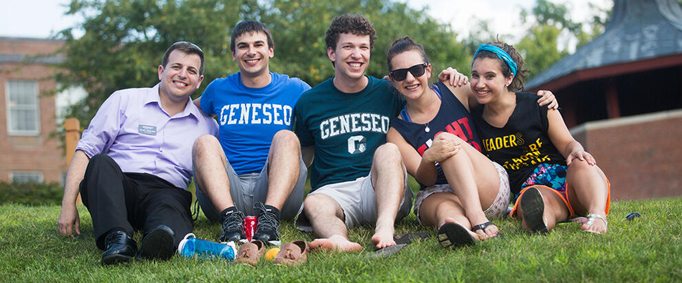 college students sitting on the lawn with arms around each other smiling