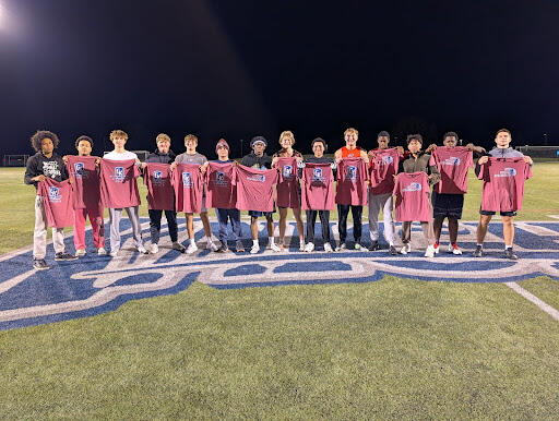 A group of people standing on a sports field at night holding red “GK Intramural Champion” T-shirts, lined up across a large logo.