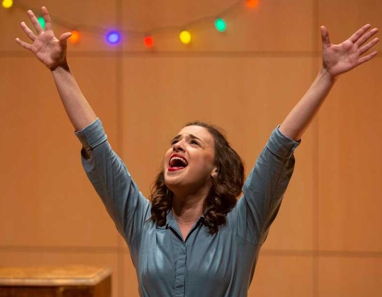 Woman with arms raised standing in front of a background decorated with colorful string lights.