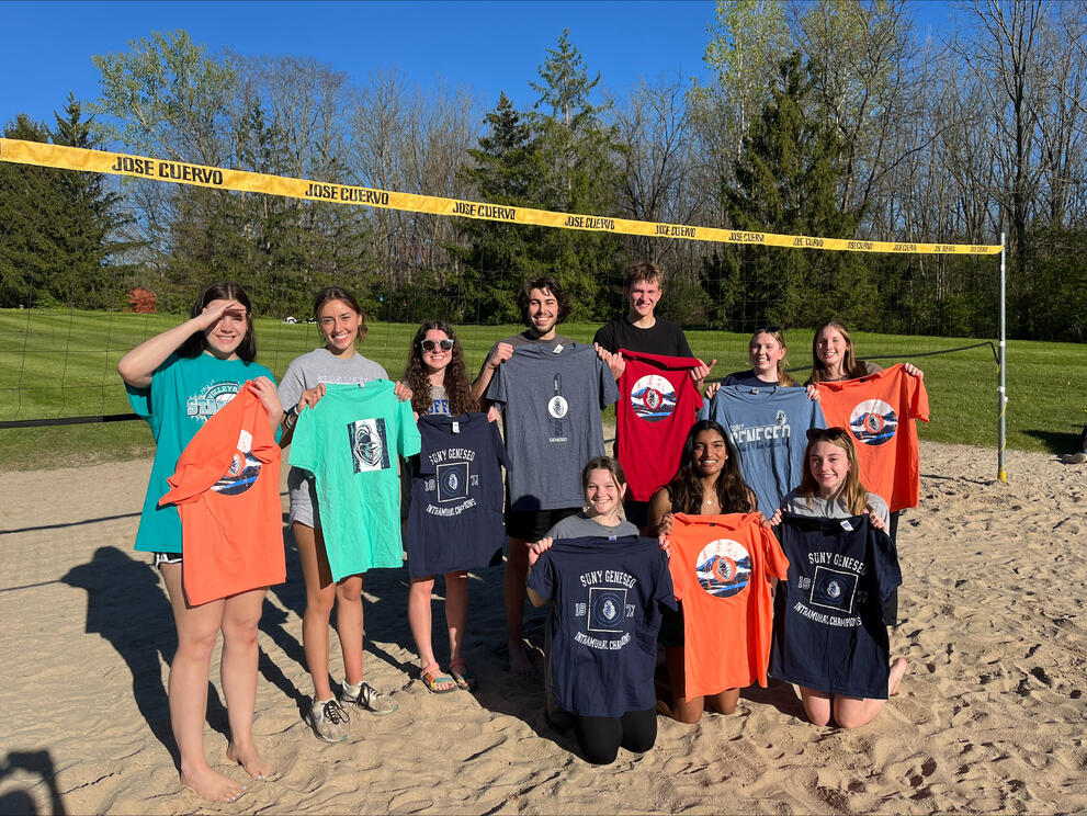 Group of sand volleyball champions holding blue, orange, and green intramural t-shirts.