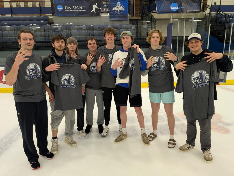 group of students, on the ice, wearing grey intramural t shirts, holding up four fingers