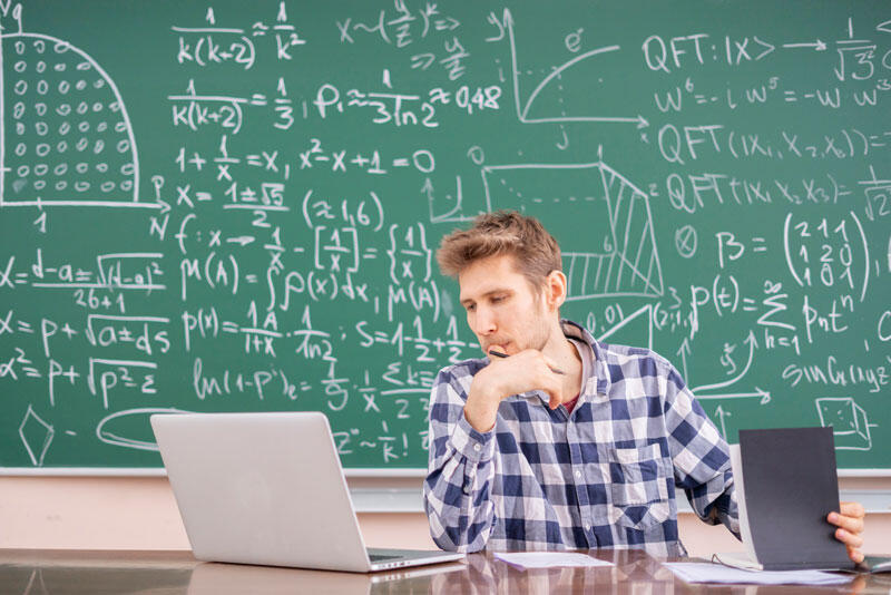 board covered with equations and man sitting with laptop