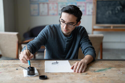 Mark Moroz '27 uses a pen in dipped ink to create an illustration of a tree.