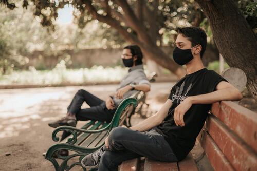 Men wearing masks sitting on park benches