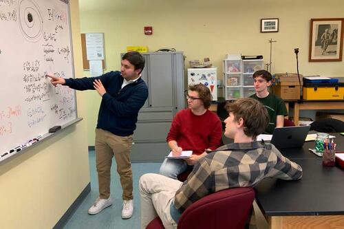 students at white board discuss physics