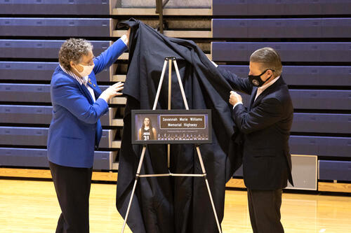 2 government representatives remove black drape from sign