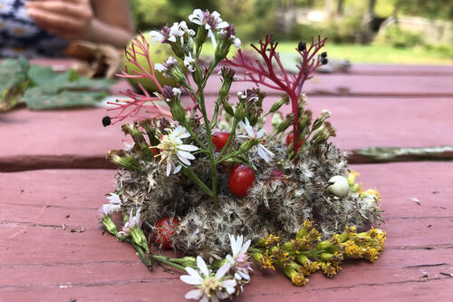 flowers, plants and other foliage is arranged artfully on a picnic table.