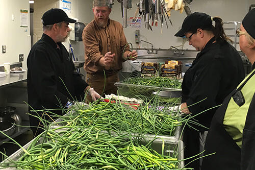 Dan DeZarn talks to CAS employees as they process garlic scapes in the kitchen.