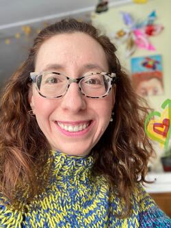 headshot of Hinda Mandell, wearing a colorful sweater, glasses and smiling
