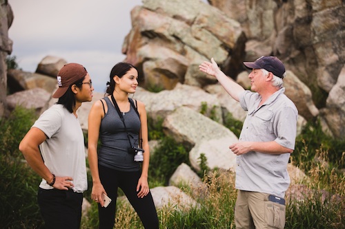 Professor Jim Kernan speaks with two students next to rocks