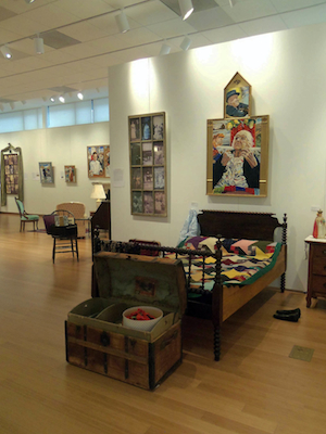 A museum exhibit of a woven quilt and the painting of the author's grandmother.