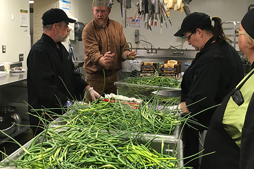 Dan DeZarn talks to CAS employees as they process garlic scapes in the kitchen.