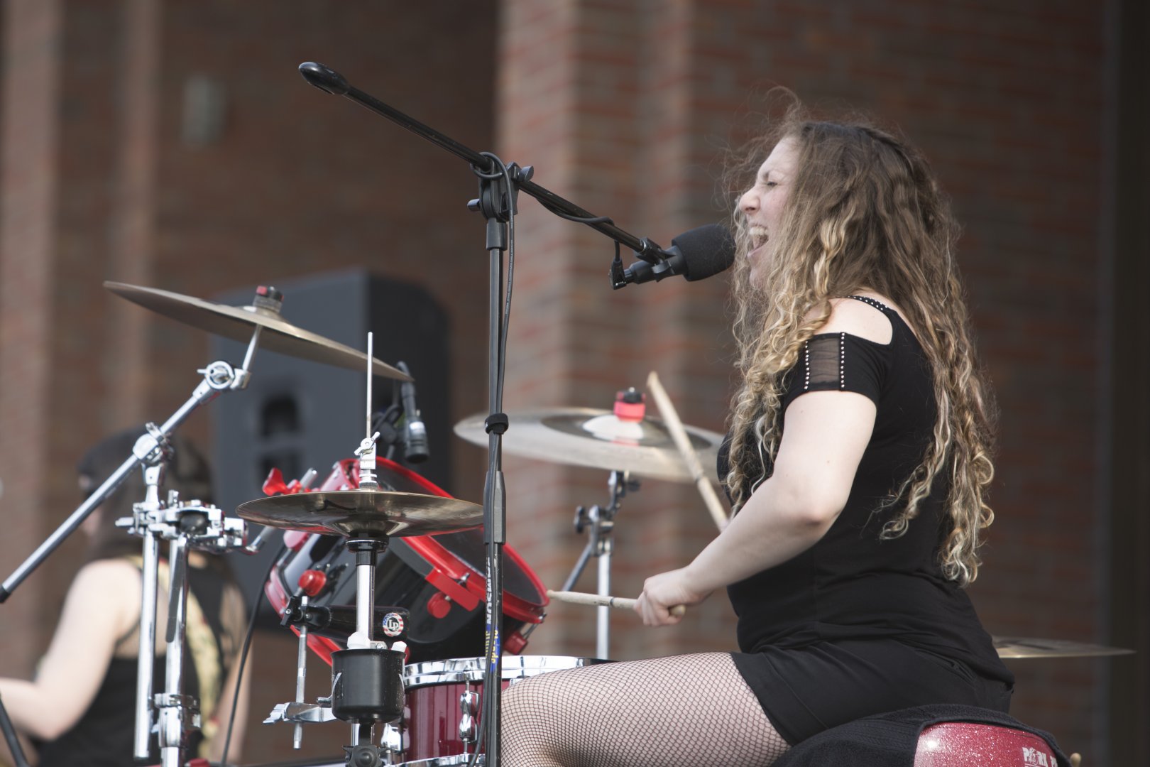A photo of one of Jackknife Stiletto's members, singing and playing the drums.