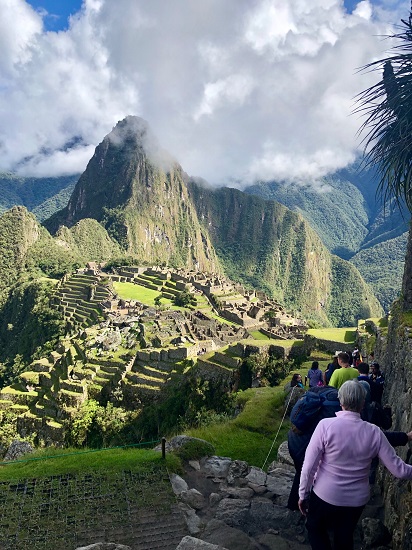 Tourists overlooking the ancient Incan city of Machu Picchu surrounded by lush green mountains and dramatic clouds. Tourists overlooking the ancient Incan city of Machu Picchu surrounded by lush green mountains and dramatic clouds.