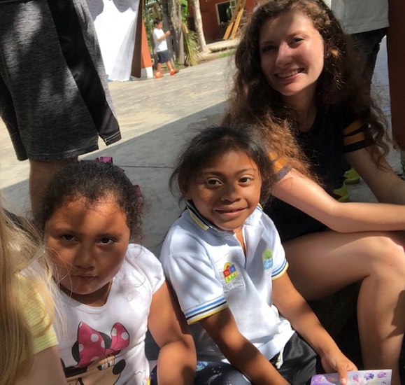 A smiling woman sits with two young Mexican girls, all enjoying time together outdoors on a sunny day. A smiling woman sits with two young Mexican girls, all enjoying time together outdoors on a sunny day.