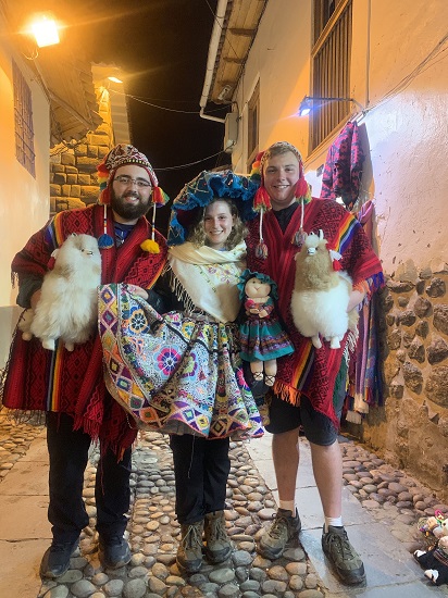 Three people wearing traditional Andean clothing, including red ponchos and a colorful layered skirt, and holding llama dolls. Three people wearing traditional Andean clothing, including red ponchos and a colorful layered skirt, and holding llama dolls.