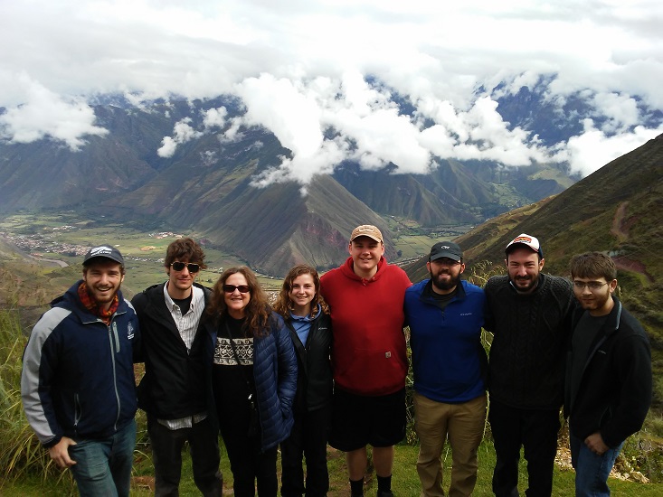 A group of people posing together outdoors with a mountainous landscape and clouds in the background. A group of people posing together outdoors with a mountainous landscape and clouds in the background.