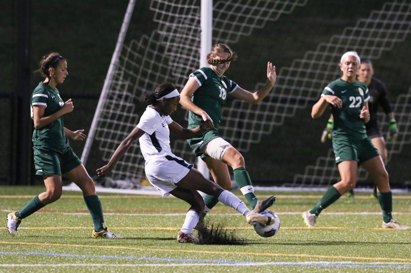 A SUNY Geneseo women's soccer player kicking the ball towards the goal while guarded by other players A SUNY Geneseo women's soccer player kicking the ball towards the goal while guarded by other players