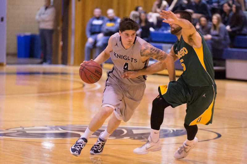 A SUNY Geneseo men's basketball player dribbling while blocking off another player A SUNY Geneseo men's basketball player dribbling while blocking off another player
