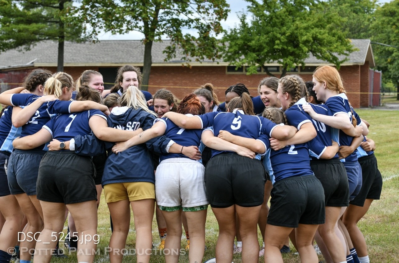 Geneseo Women's Rugby team huddling together on the field.
