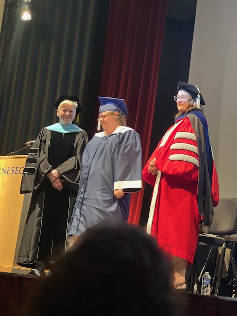 Graduating student standing on stage with two faculty members