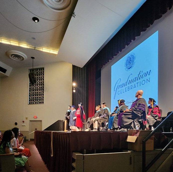 Graduating student standing on stage with group of faculty wearing caps and gowns.