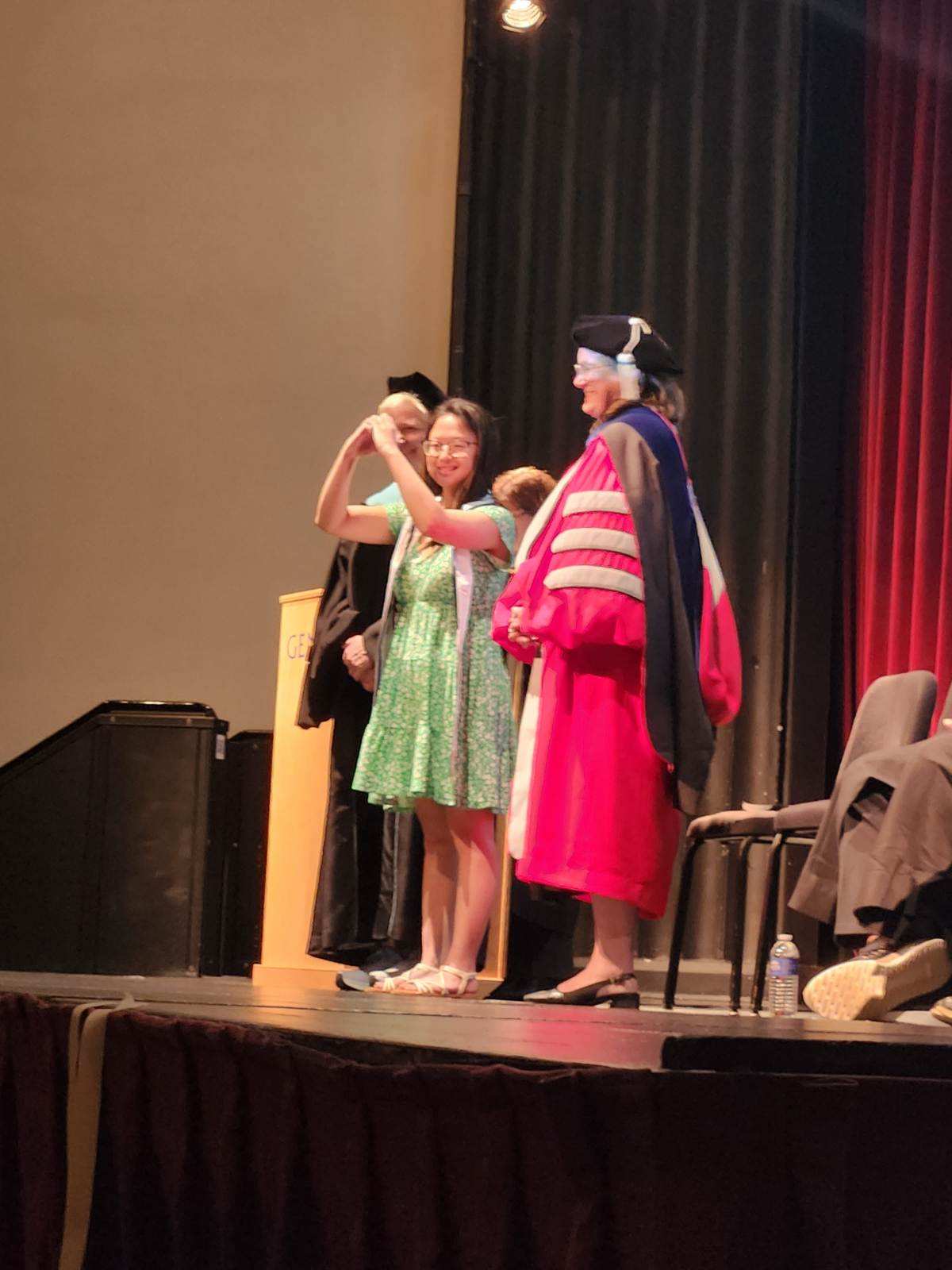 Graduating student standing on stage with two faculty members