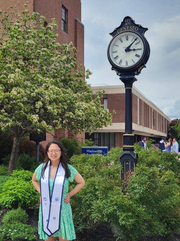 Graduate wearing a blue and white stole and smiling next to a street clock