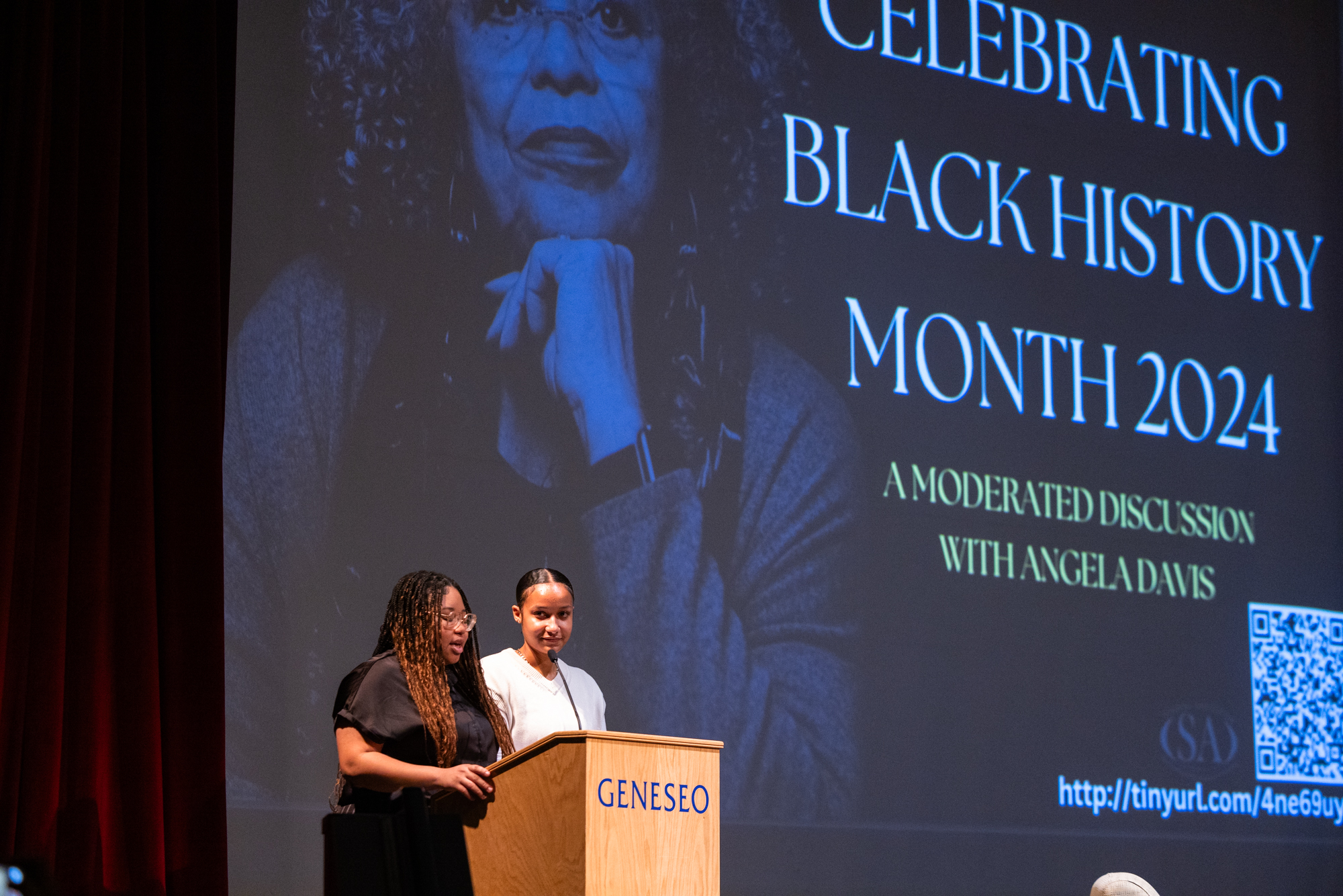Two students standing at a podium in front of a slide that reads Celebrating Black History Month 2024