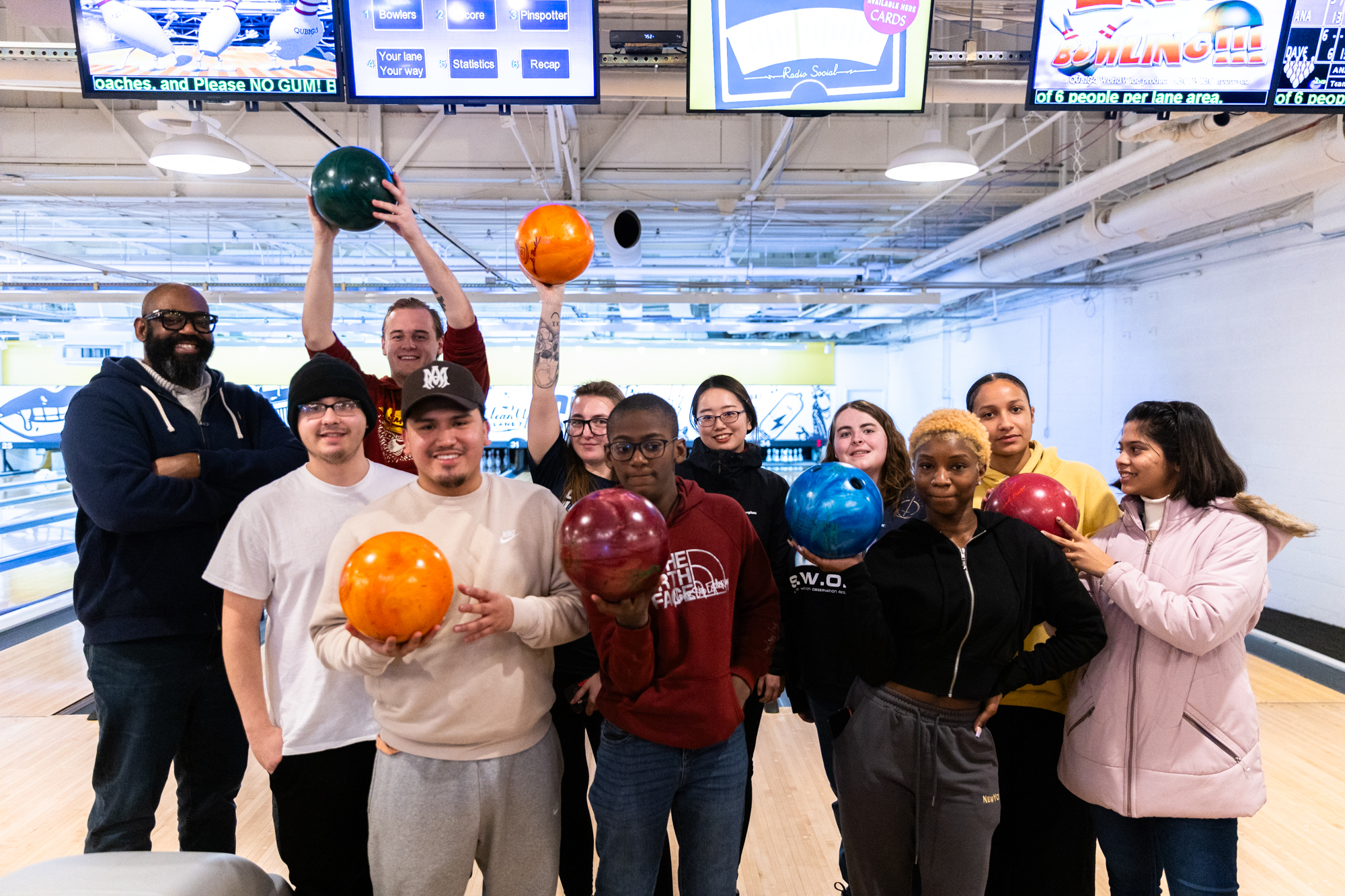 Group of students holding bowling balls in a bowling alley.