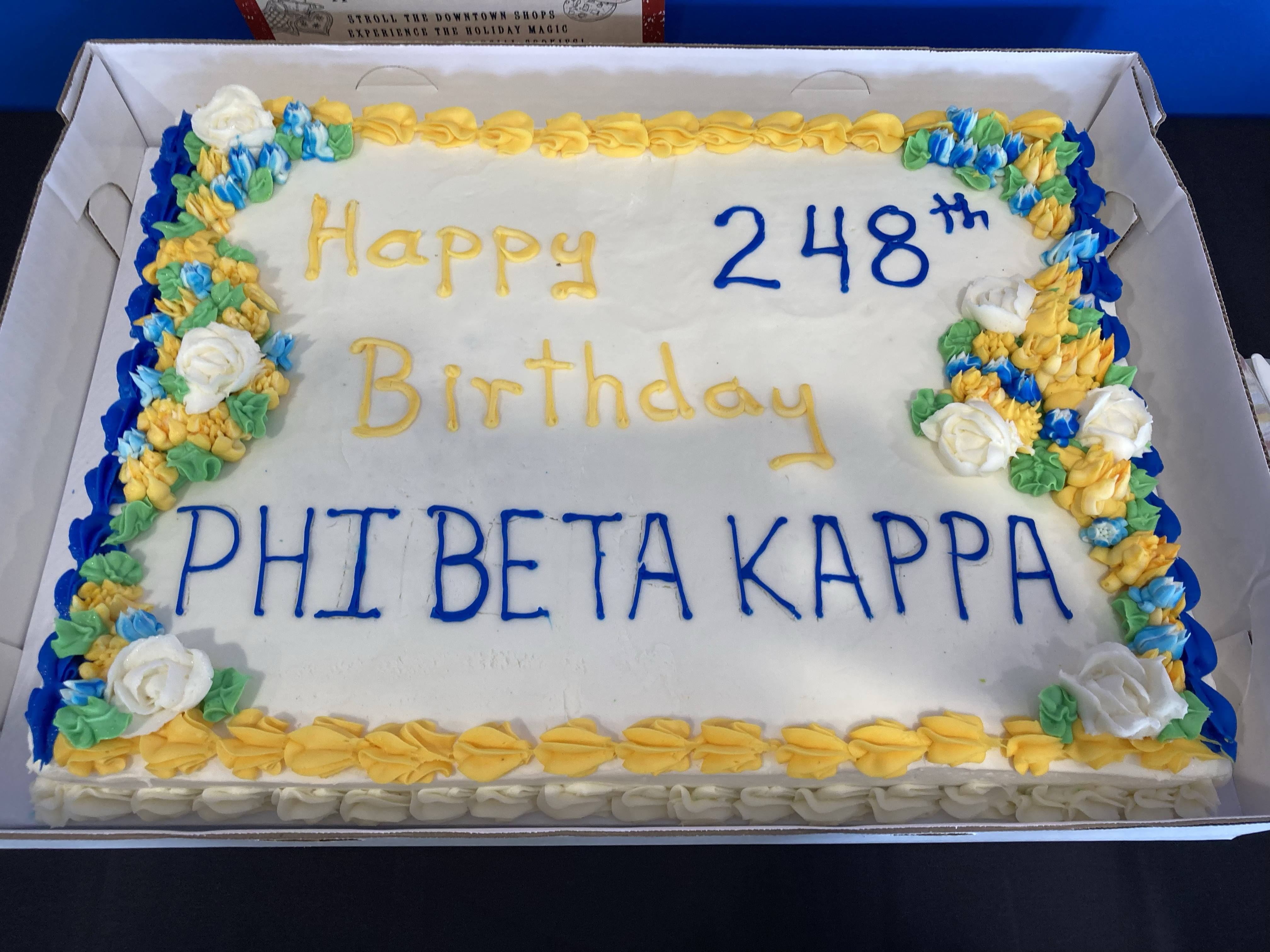 Sheet cake with white icing and yellow and blue decorations; lettering reads