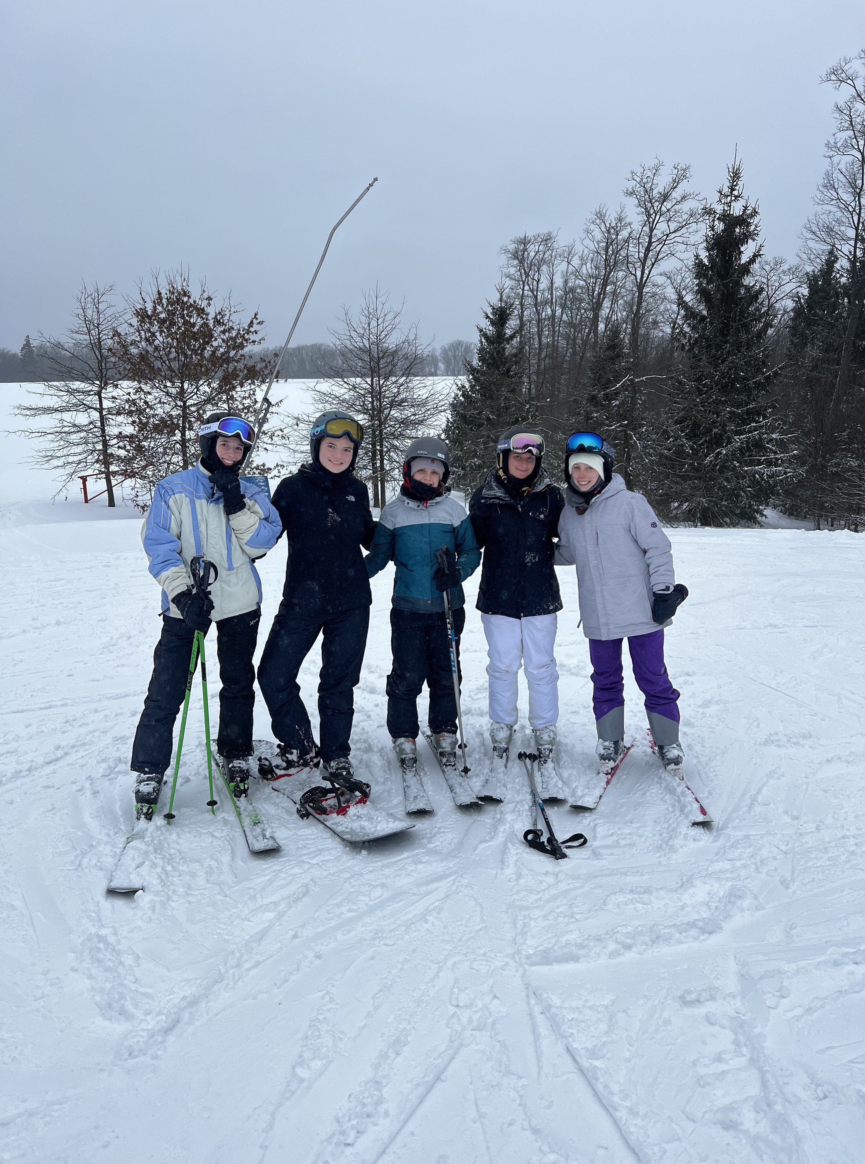 Group of students in snow gear, with skis and snowboard, posing together
