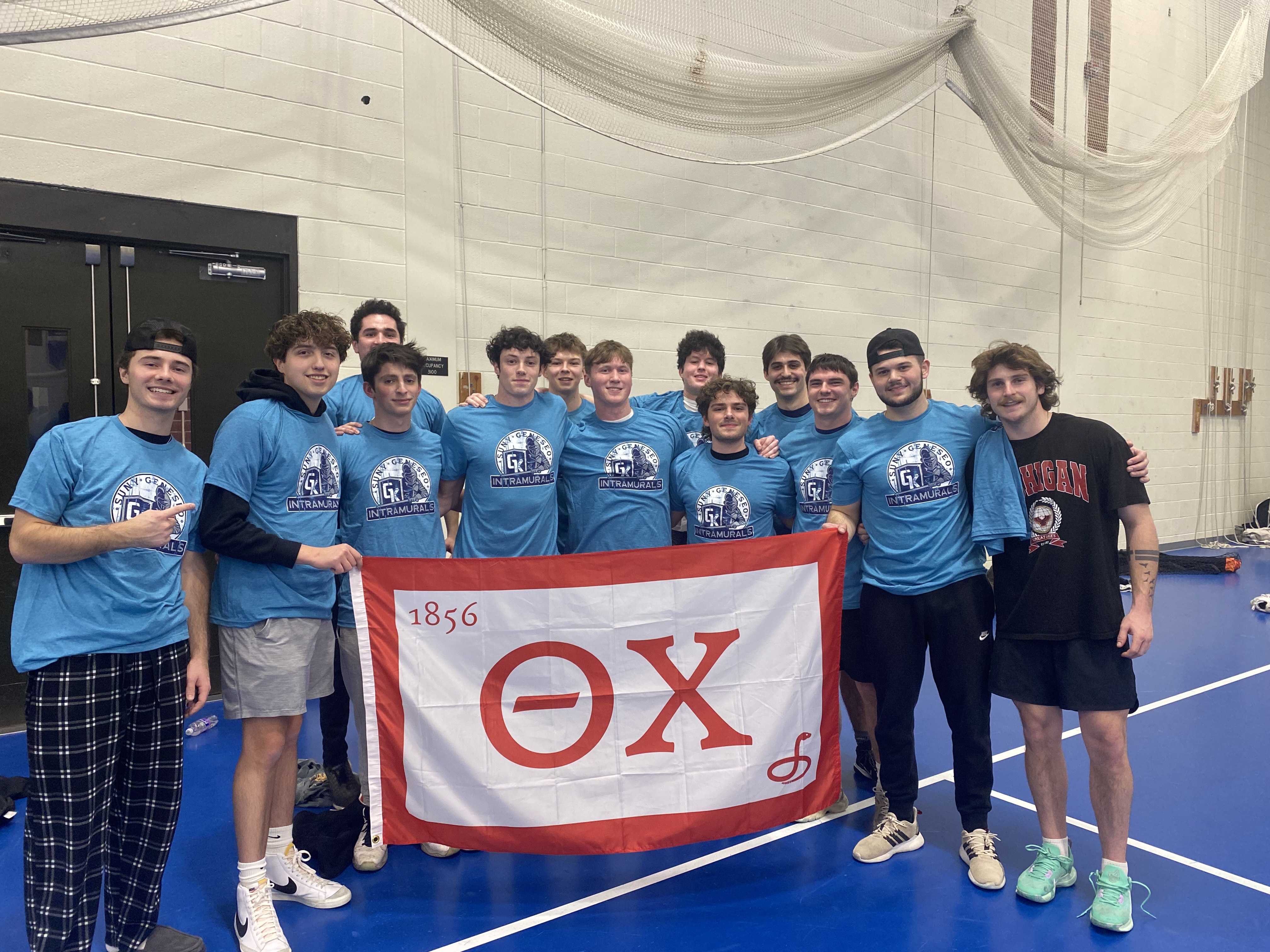 group of students, wearing blue intramural shirts, holding a theta chi fraternity flag