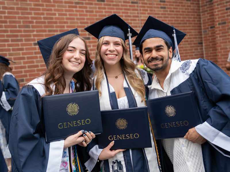 three graduates holding diplomas