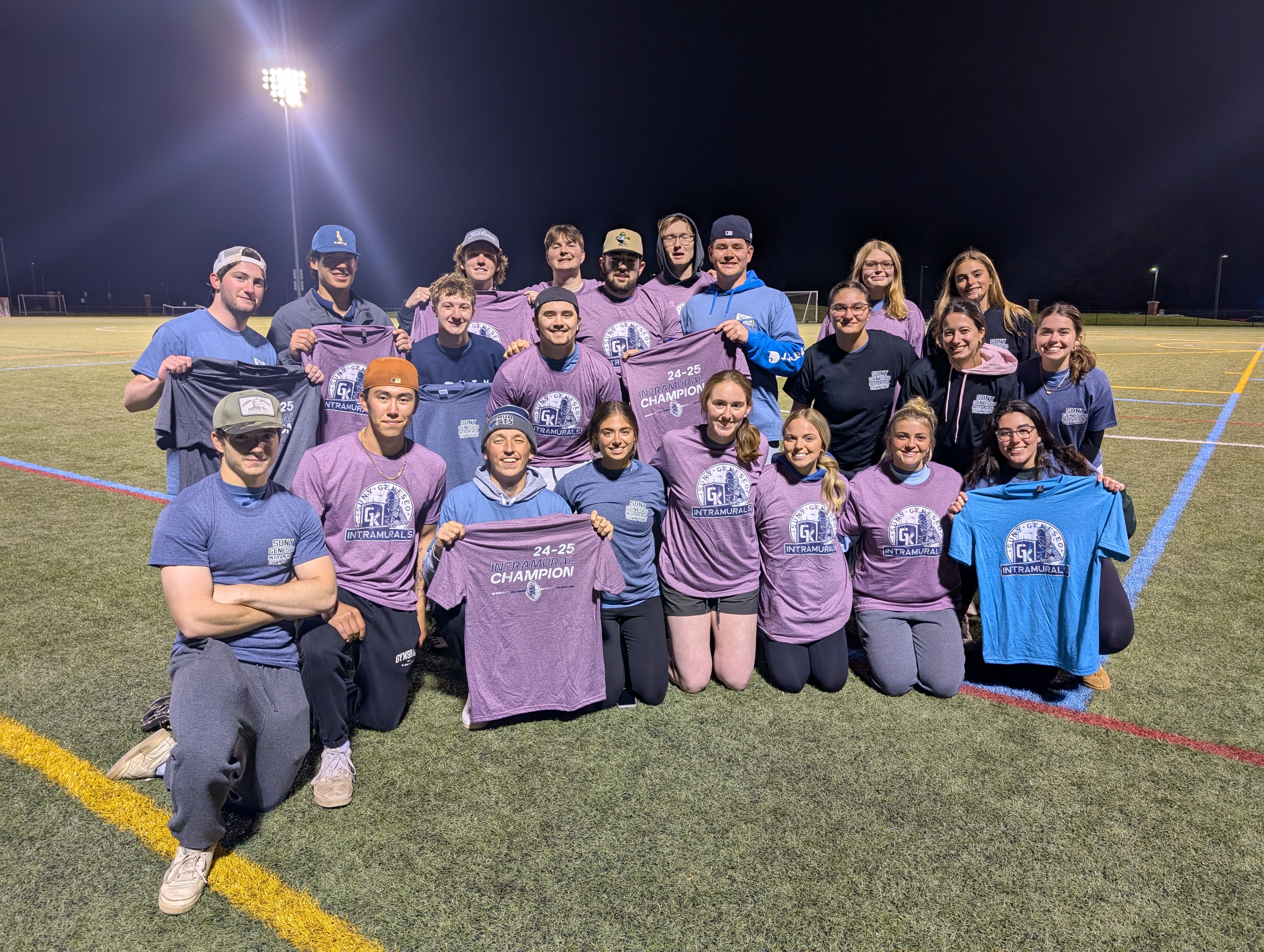 group of students outside on the turf at night. maroon shirts, blue shirts.