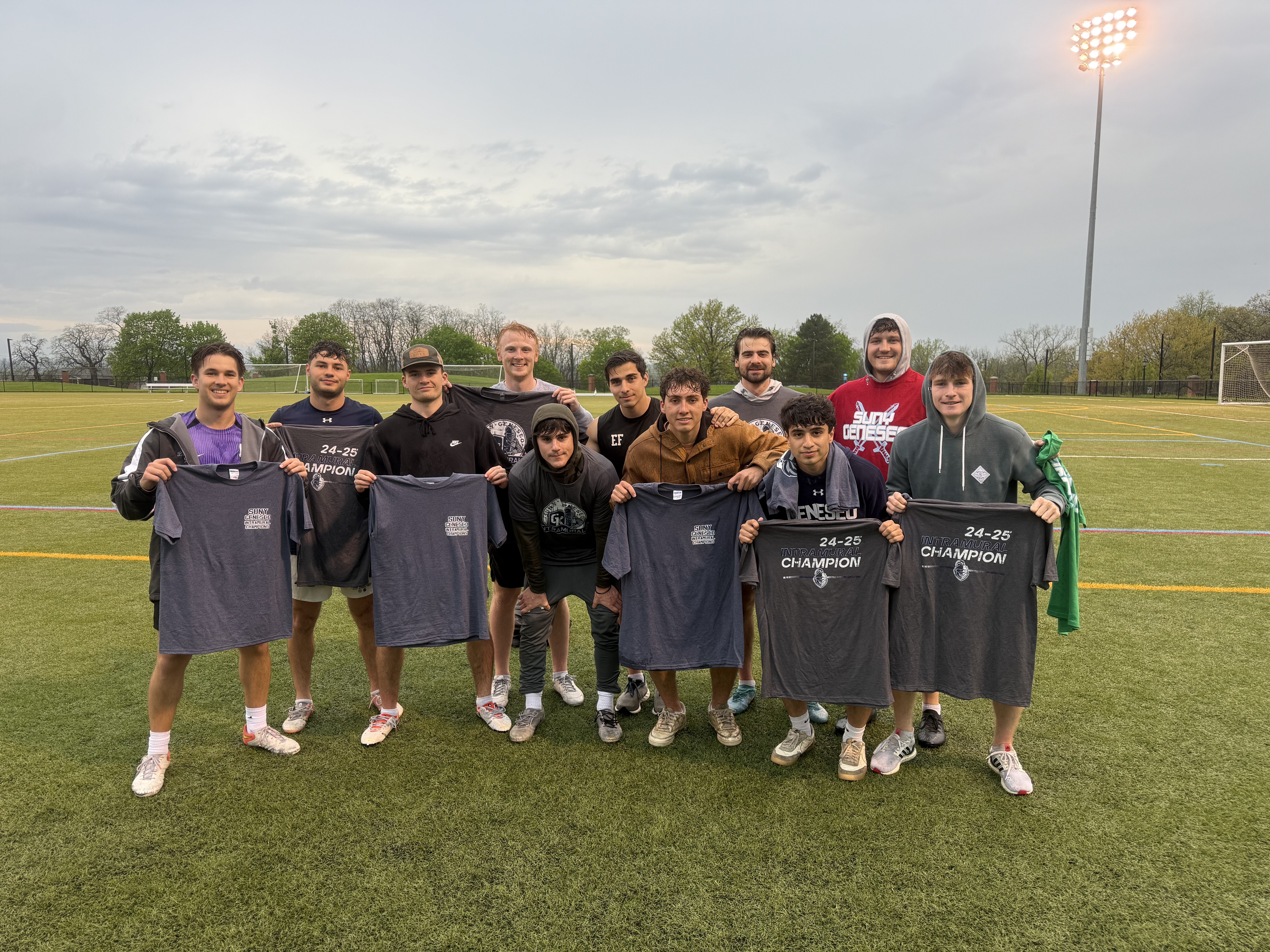 group of students outside on the turf. holding up grey champ shirts