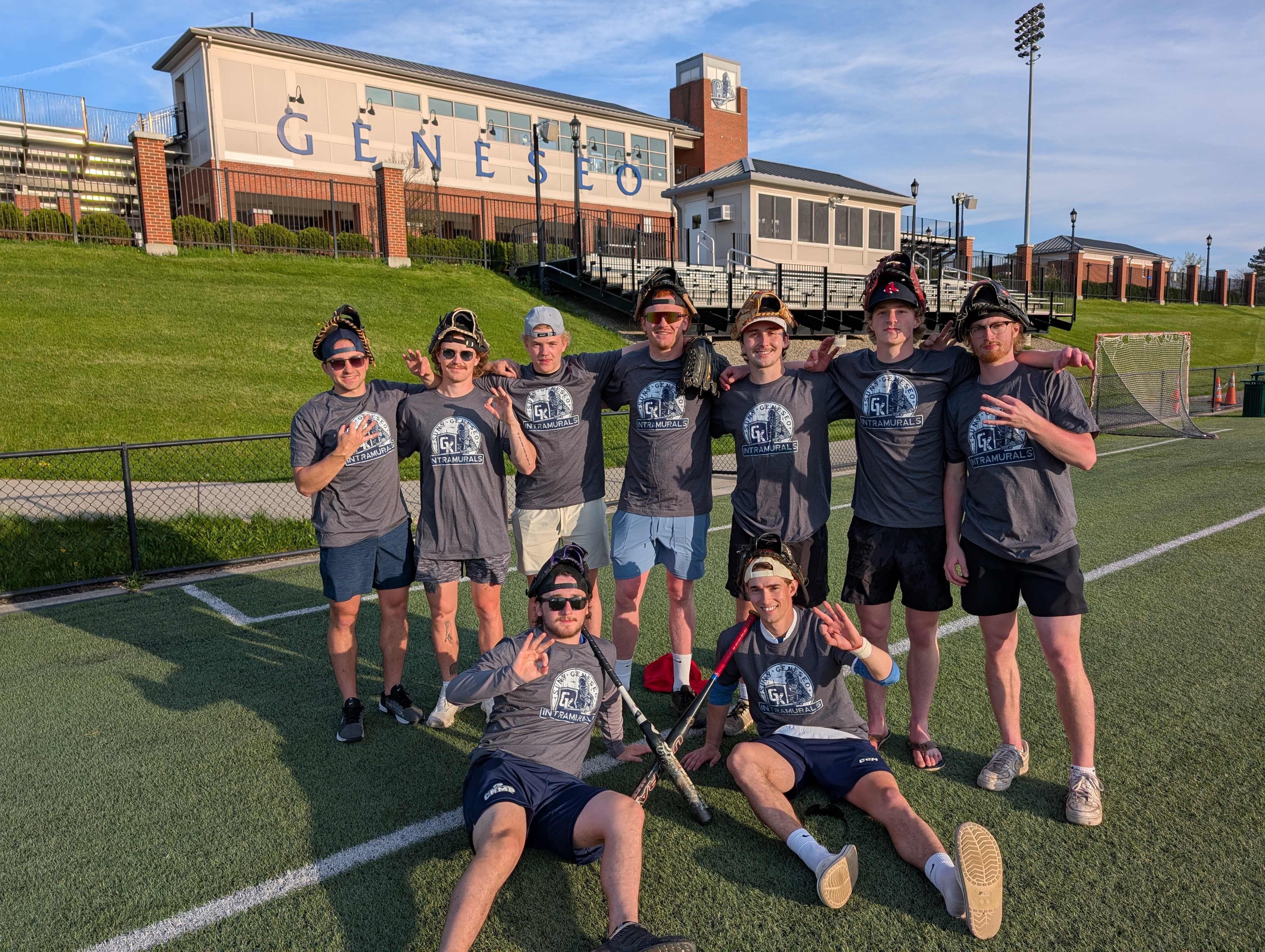 group of students outside on the turf. grey champ shirts and wearing baseball gloves on head.