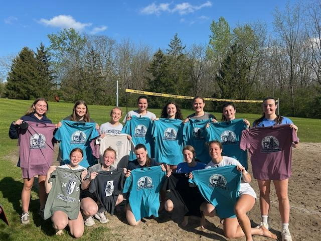 group of students on the sand volleyball court holding up blue and maroon t shirts