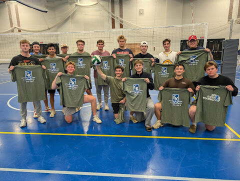 A group of students posing on an indoor volleyball court holding green “GK Intramural Champion” T-shirts, with a volleyball net in the background.