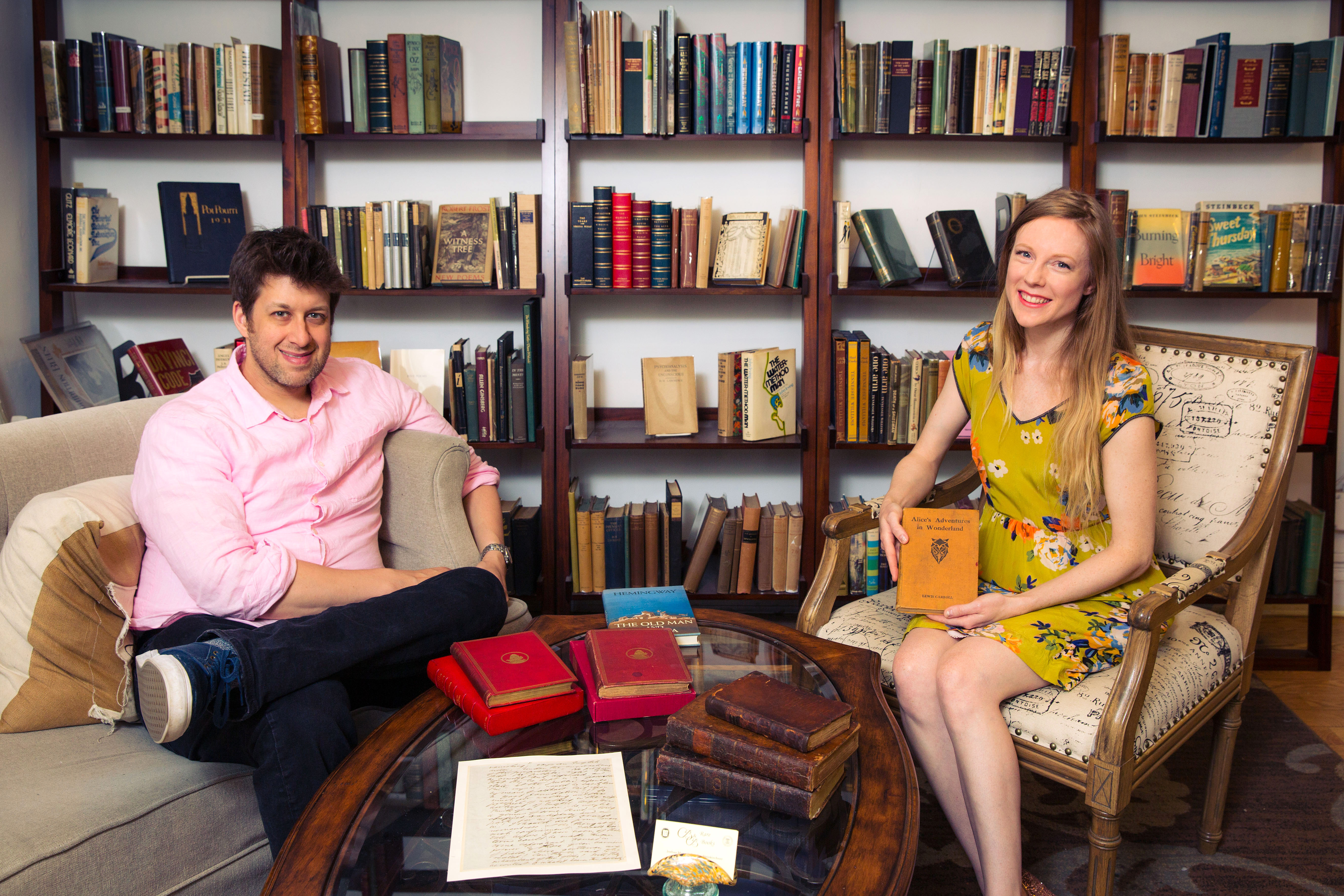 The owners of B and B Rare Books hold a copy of a rare book and sit on couches in their gallery.